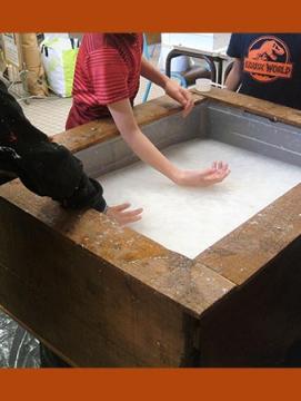 Photographie d'une étape de fabrication du papier, dans le cadre en bois appelé "forme"