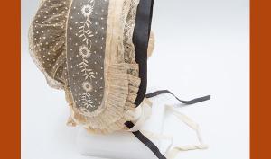 Coiffe en tulle de coton rebrodé de plumetis et de broderies blanches, volant de dentelle au fuseau orné de plis plats avec une sous coiffe de couleur noire.