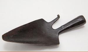 Outil en fer forgé, en forme de petite pelle pointue avec un crochet à droite. Le manche est manquant.