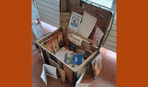 Malle en bois, présentée ouverte, avec à l'intérieur des documents sur le livre "Les Clients du bon Chien jaune".