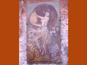 Enseigne peinte de l'Auberge de l'Œuf Dur : une danseuse vêtue d'une robe vaporeuse tient devant elle un grand œuf