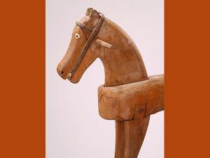 Avant-main d'un cheval à bascule en bois, des deux côtés de la tête se trouve une poignée. Les yeux sont en relief et leur tour est peint en blanc, le filet rudimentaire a été réalisé en cuir.