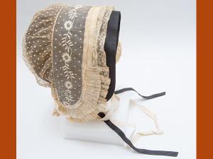 Coiffe en tulle de coton rebrodé de plumetis et de broderies blanches, volant de dentelle au fuseau orné de plis plats avec une sous coiffe de couleur noire.