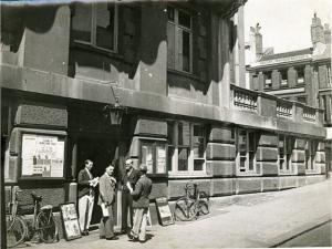 Vue de Londres, datée de 1934 : groupe d'hommes à l'entrée d'un bâtiment administratif. Photographie rapportée de Londres par Pierre Mac Orlan à l'occasion d'un de ses reportages.