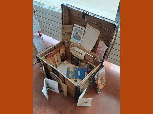 Malle en bois, présentée ouverte, avec à l'intérieur des documents sur le livre "Les Clients du bon Chien jaune".