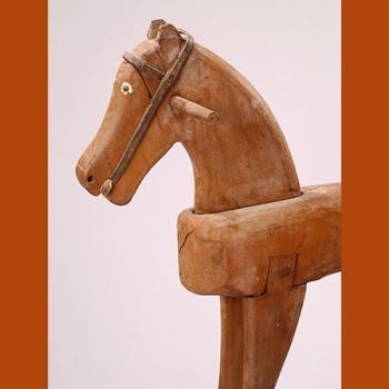Avant-main d'un cheval à bascule en bois, des deux côtés de la tête se trouve une poignée. Les yeux sont en relief et leur tour est peint en blanc, le filet rudimentaire a été réalisé en cuir.