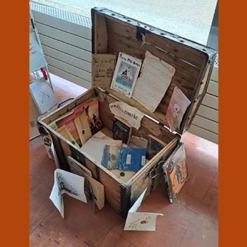 Malle en bois, présentée ouverte, avec à l'intérieur des documents sur le livre "Les Clients du bon Chien jaune".