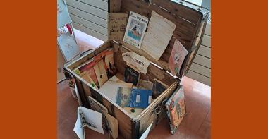 Malle en bois, présentée ouverte, avec à l'intérieur des documents sur le livre "Les Clients du bon Chien jaune".