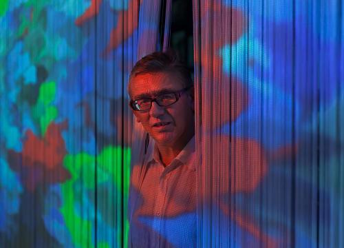 Portrait du plasticien Miguel Chevalier, il apparaît par l'ouverture de rideaux au milieu d'une œuvre projetée